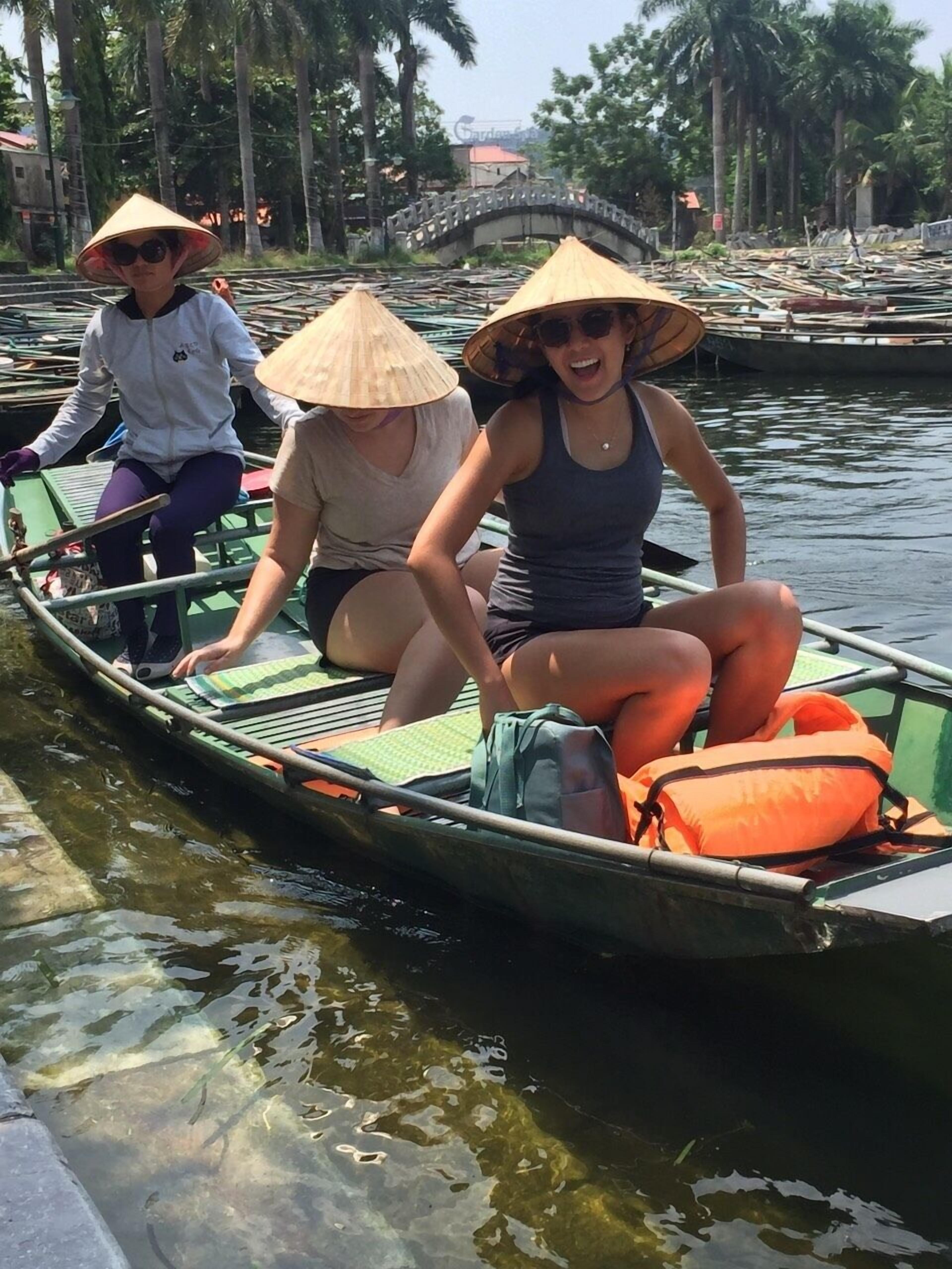 Three people in a narrow boat with a bridge in the background.