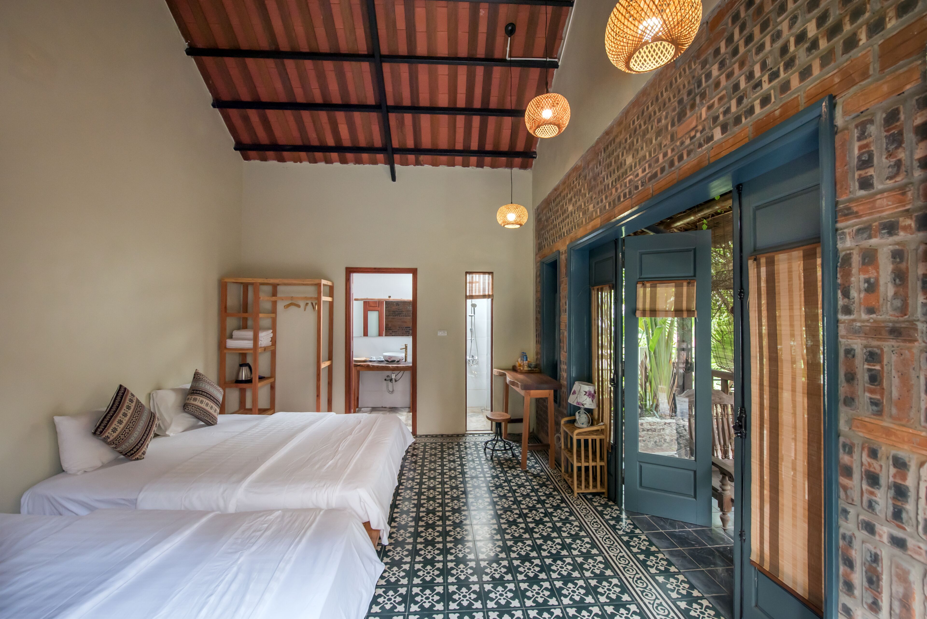 Una habitación con dos camas, un armario de madera, una mesita con una silla y una puerta que da al exterior.