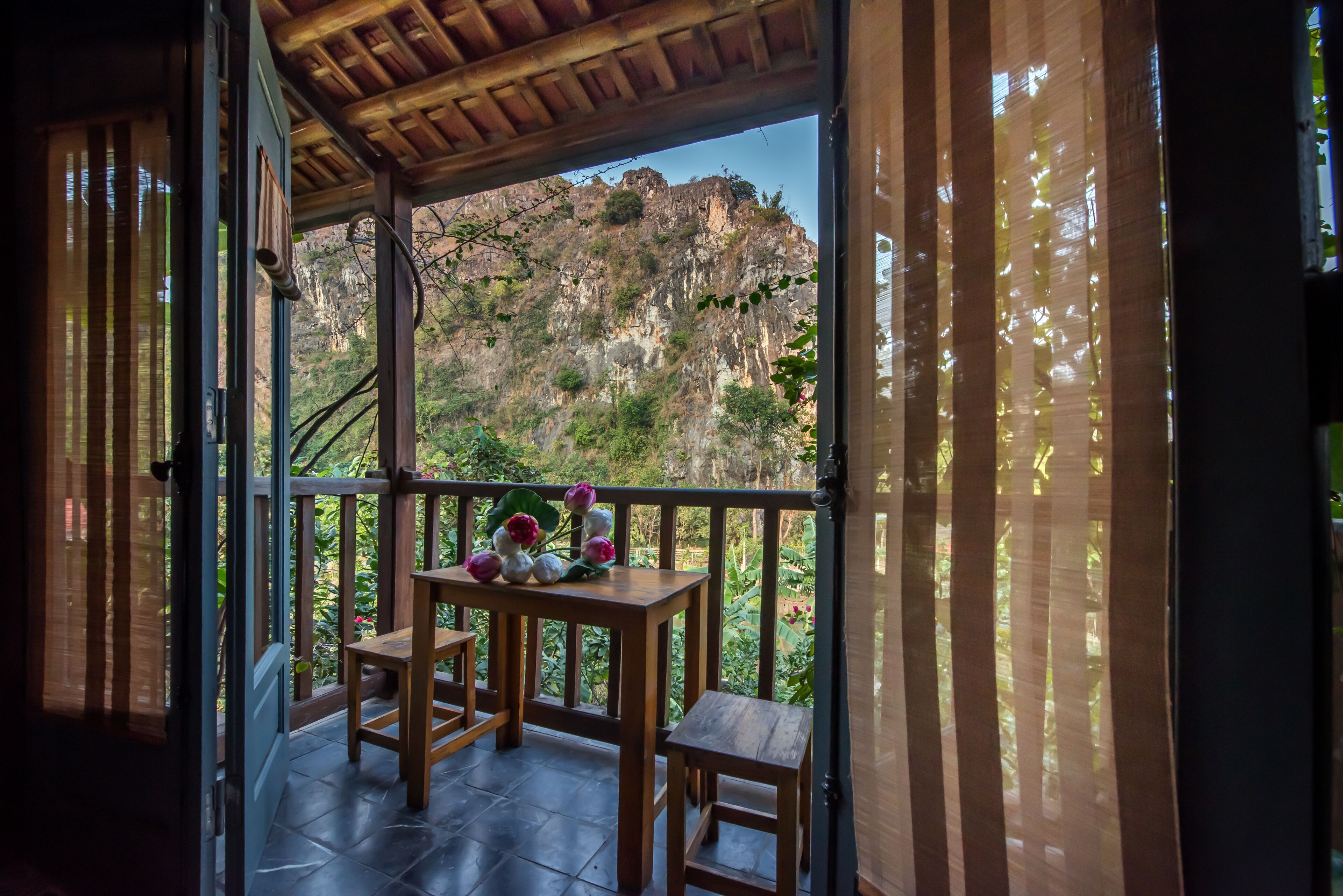 A wooden balcony with a table and chairs, overlooking a mountainous landscape.