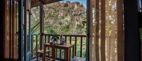 A wooden balcony with a table and chairs, overlooking a mountainous landscape.