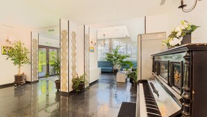 Un hall amplio con un piano de cola, plantas en macetas y un sofá azul.