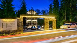 Entrada de hotel con fachada de piedra, un cartel que dice "PENSIUNE HILLTOP beauty between" y varios coches estacionados al frente.