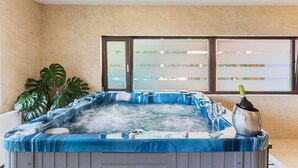Un jacuzzi con cubierta de aspecto marmolizado, una botella de champán y una planta en maceta.