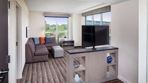 Ein modernes Wohnzimmer mit einer Couch, einem Fernseher und Blick ins Grüne.