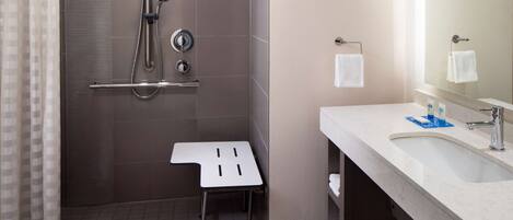 A modern bathroom with a shower, a sink, and a small stool.