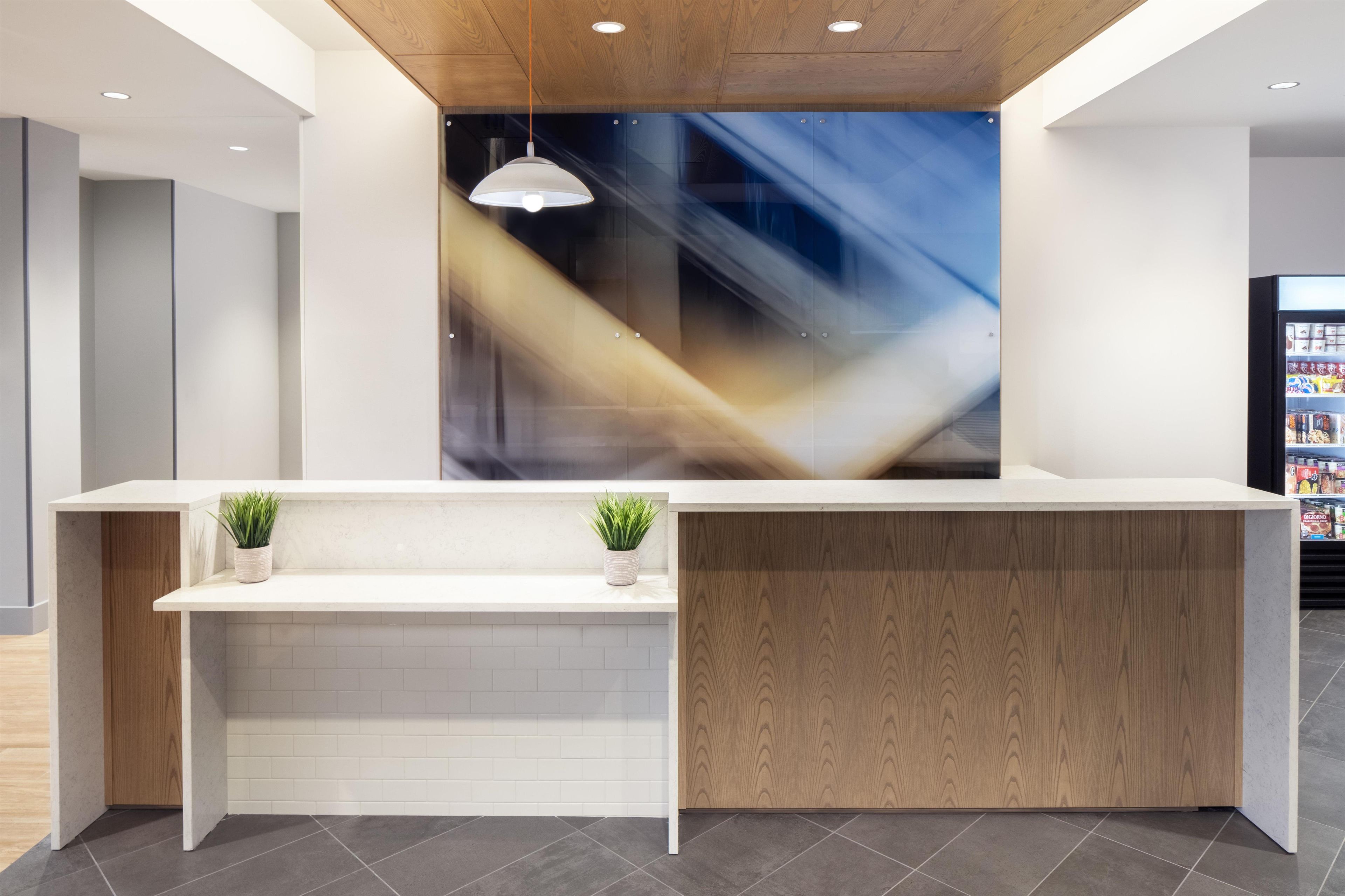 A reception desk with a modern design, featuring a wooden panel and two potted plants.
