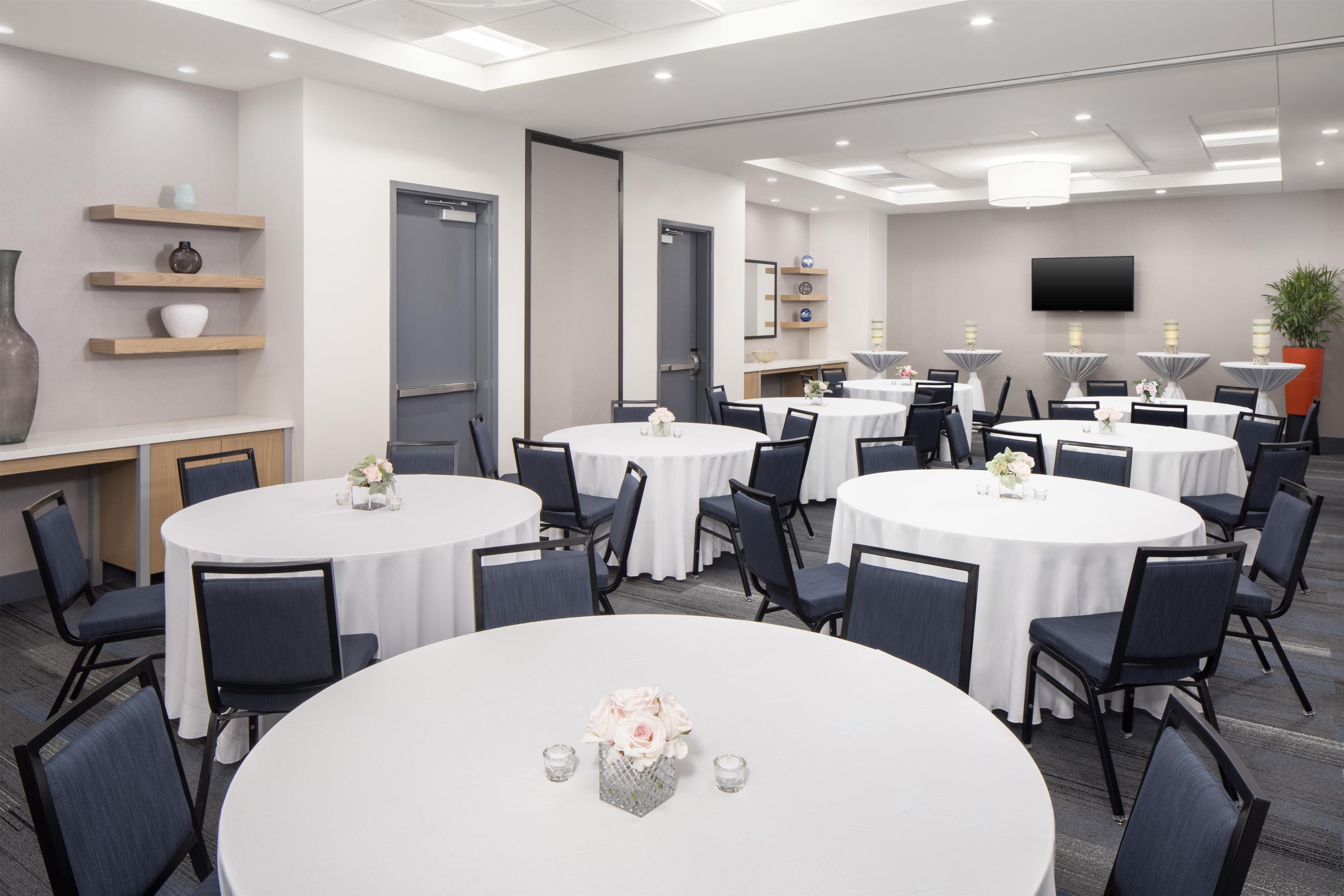 A conference room with multiple round tables, chairs, and a flat-screen TV mounted on the wall.