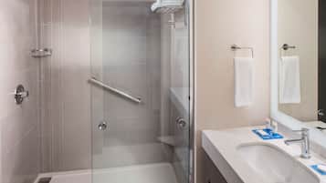 A modern bathroom with a glass shower enclosure, a sink with a mirror, and neatly folded towels on a rack.