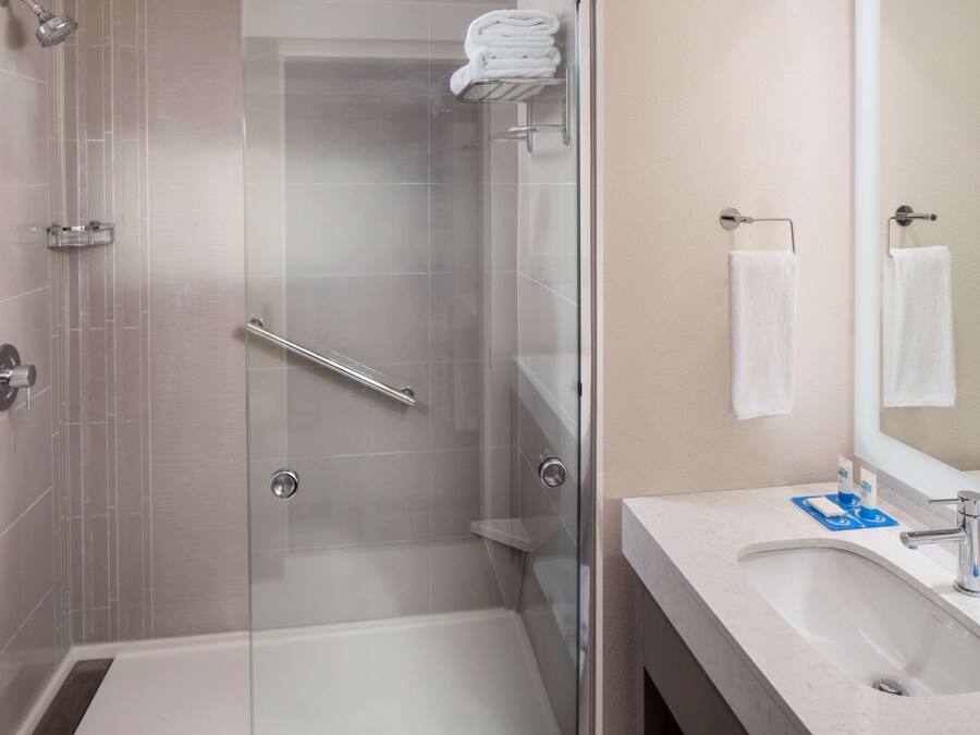 A modern bathroom with a glass shower enclosure, a sink with a mirror, and neatly folded towels on a rack.