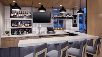 A bar area with a long counter, multiple bottles of alcohol, a television, and bar stools.
