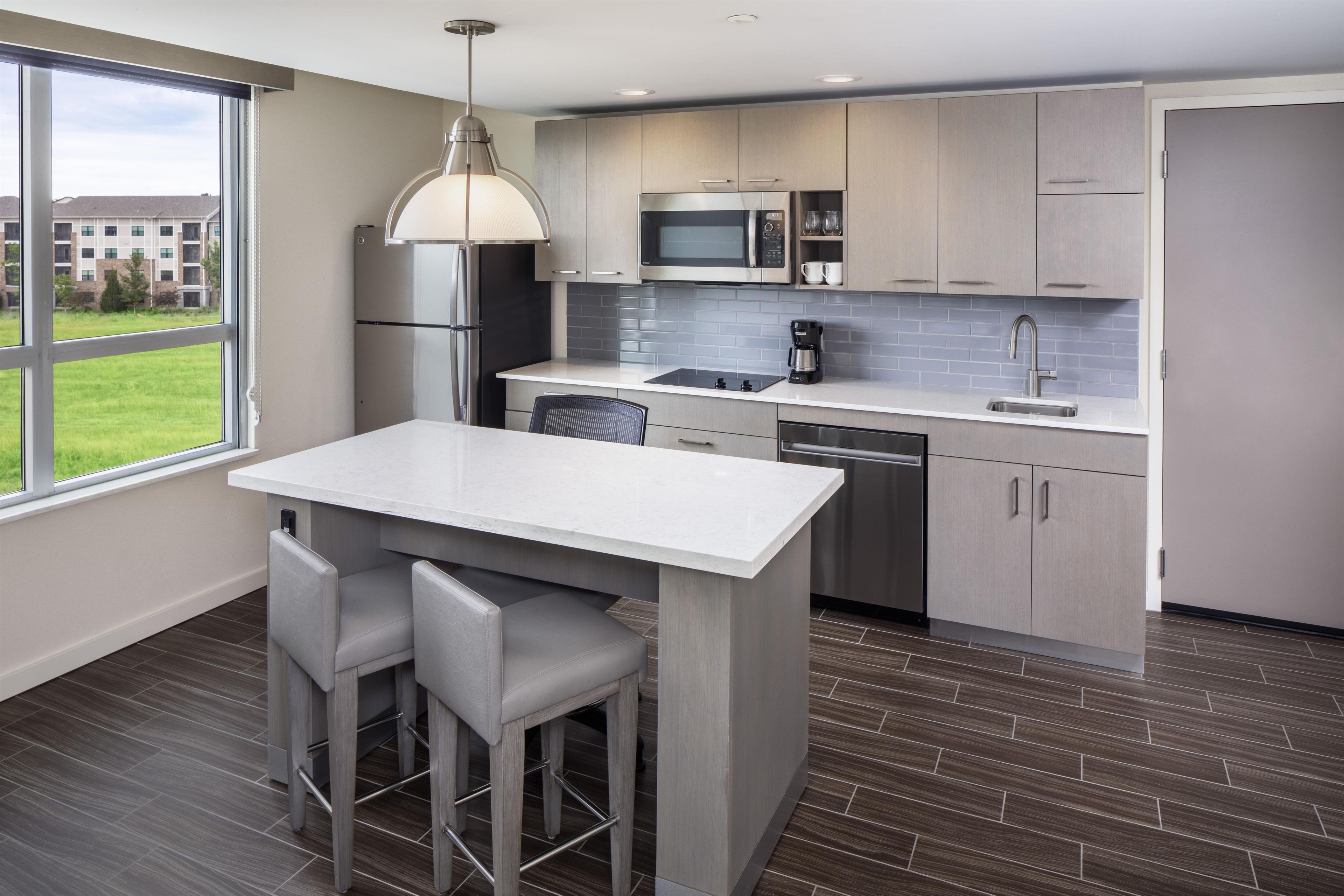 A modern kitchen with a large island, stainless steel appliances, and a view of a residential area.
