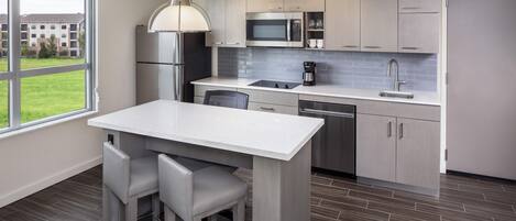 A modern kitchen with a large island, stainless steel appliances, and a view of a residential area.