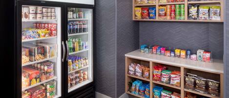 A refrigerated display case stocked with various food items and a shelf above it displaying snacks and chips.