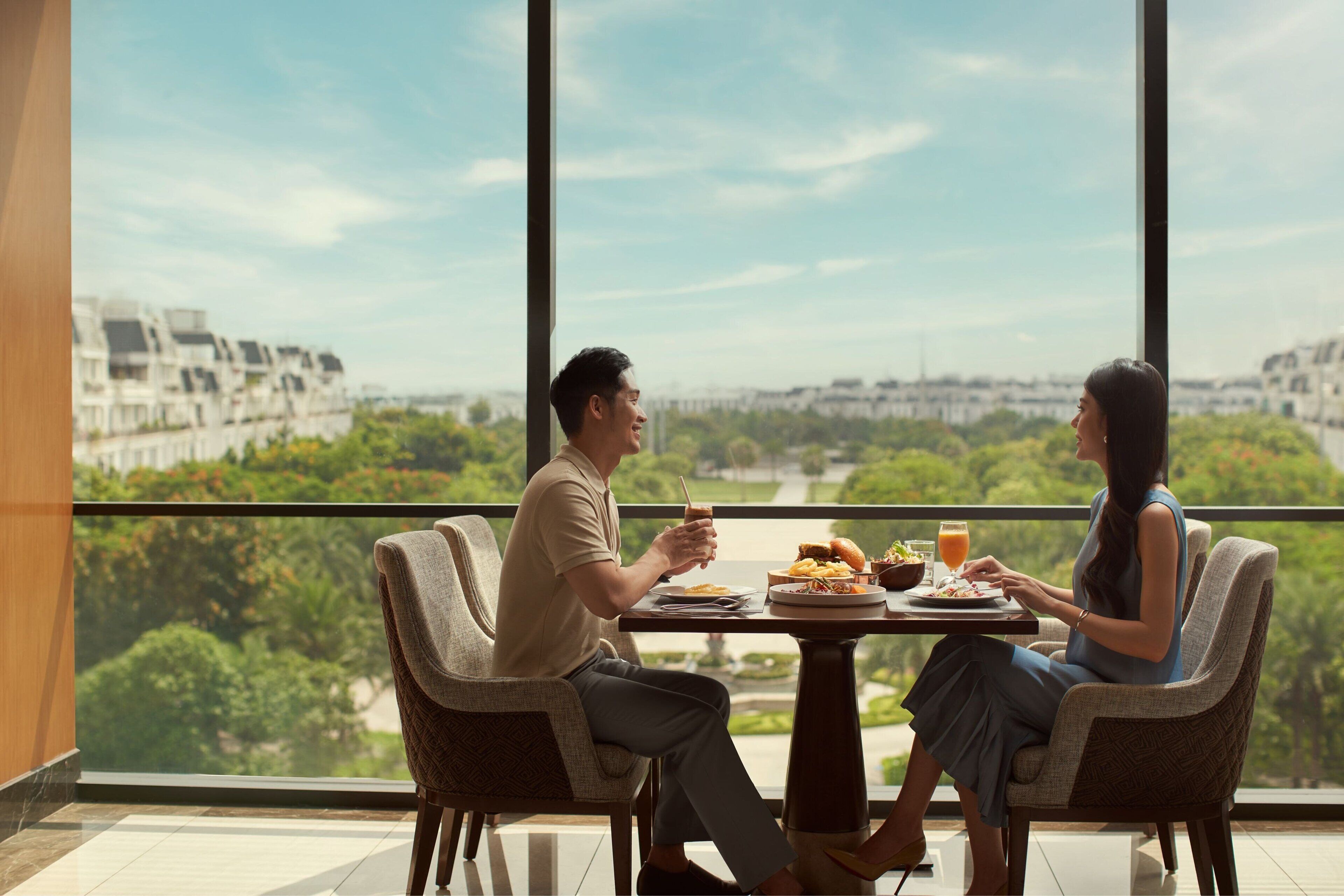 A dining area with a table set for two, overlooking a cityscape with greenery.