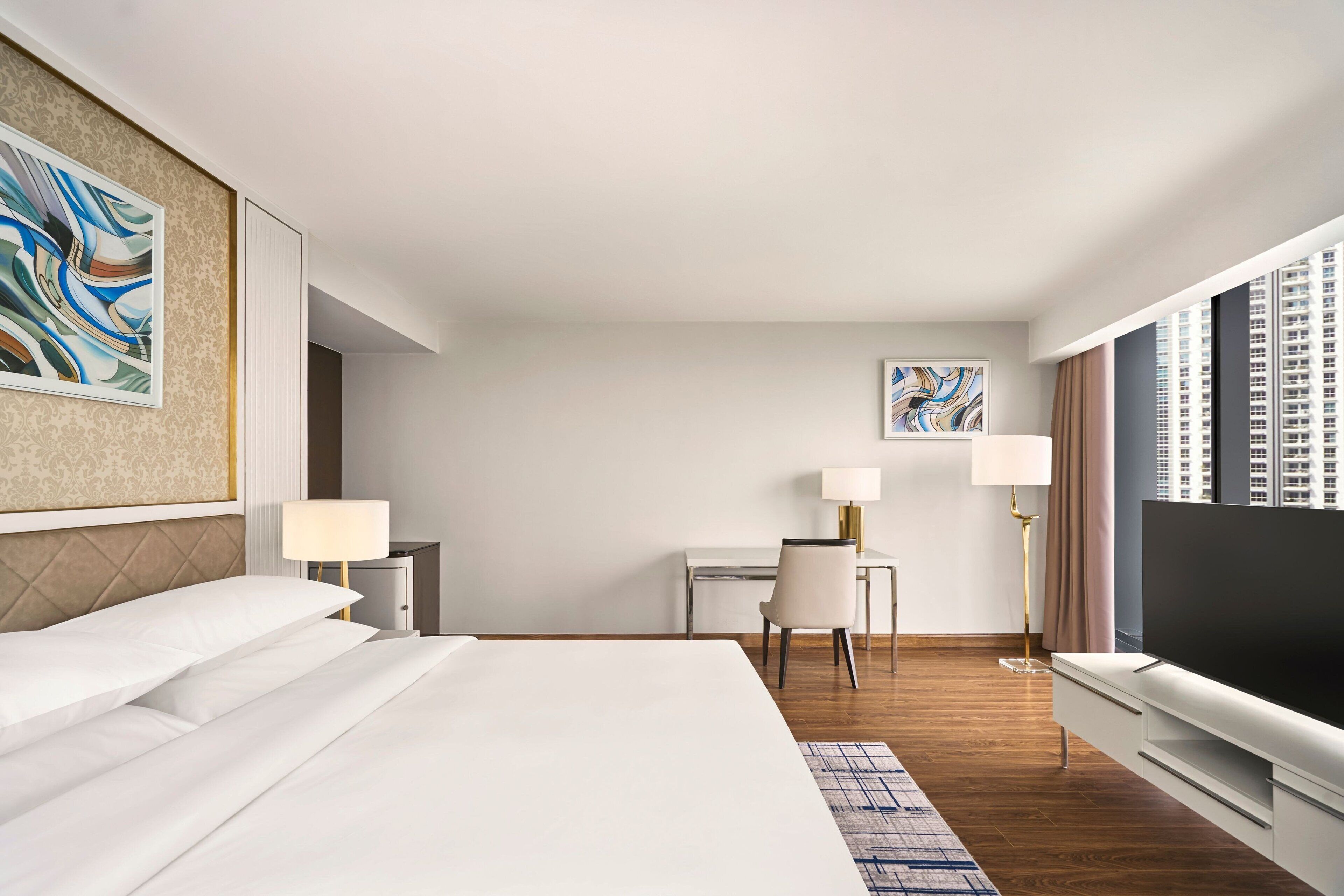 Ein Hotelzimmer mit einem großen Bett, einem Schreibtisch, einem Stuhl, einem Fernseher und Bildern an der Wand.