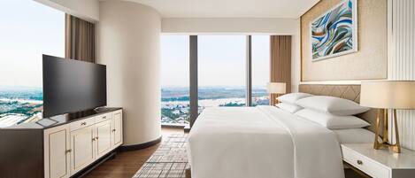 A modern hotel room with a large bed, a flat-screen TV, a desk, and a view of the city.