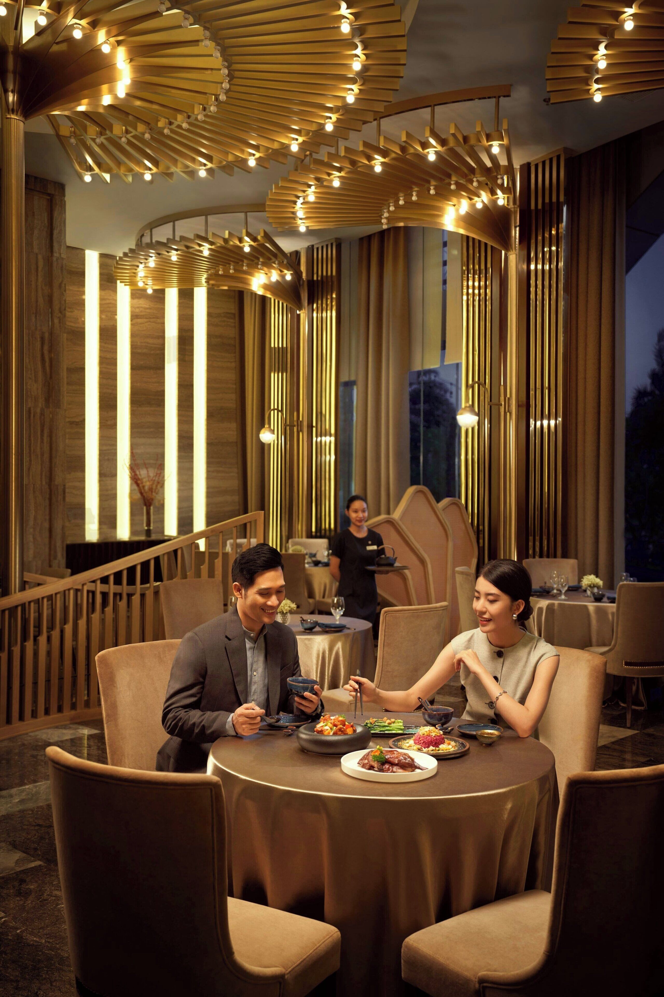 A dining area with round tables, high-backed chairs, and a modern chandelier.