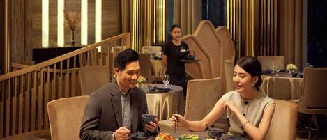 A dining area with round tables, high-backed chairs, and a modern chandelier.