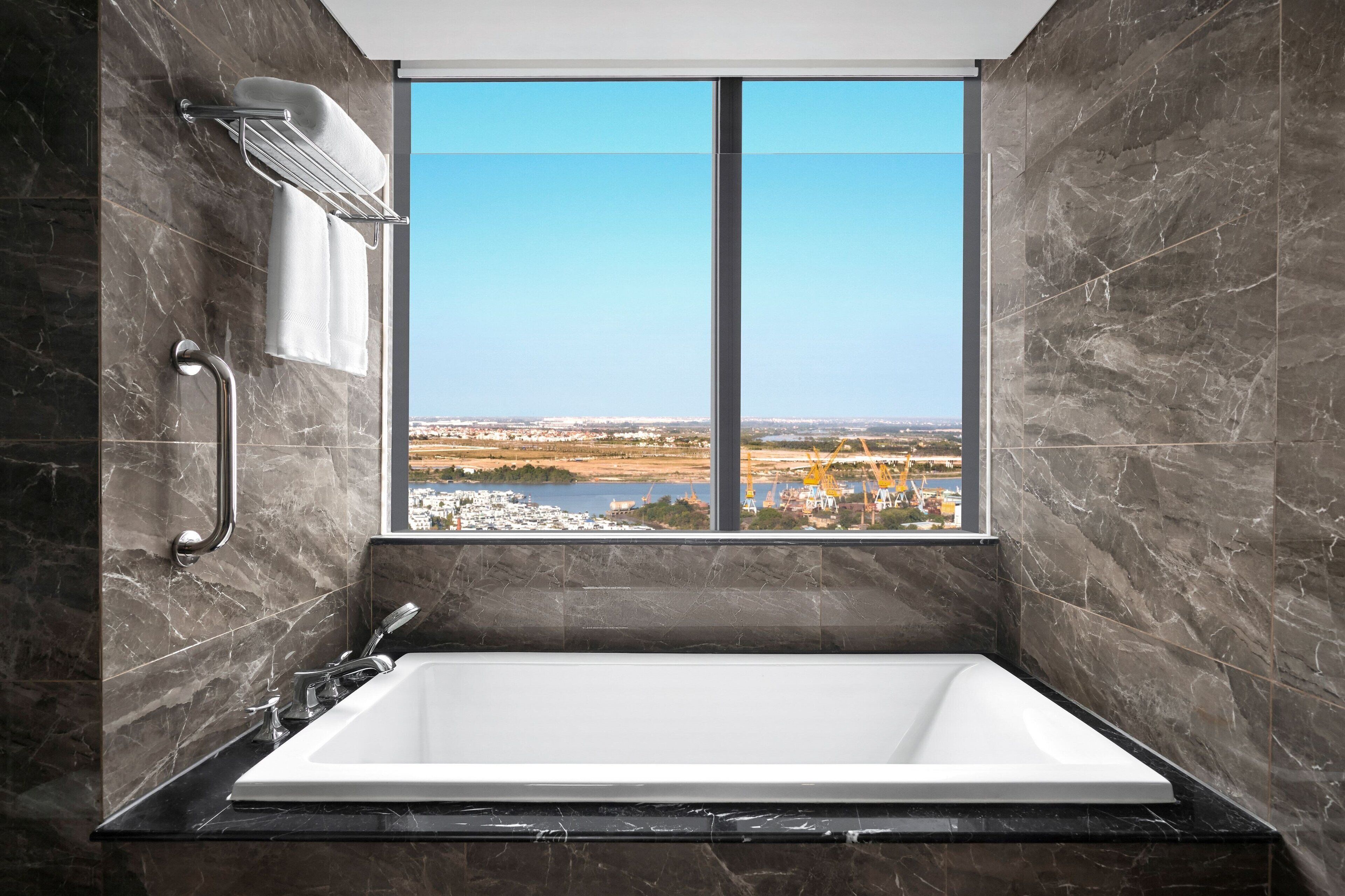 A modern bathroom with a large bathtub, a handrail, and a window offering a view of a distant landscape.