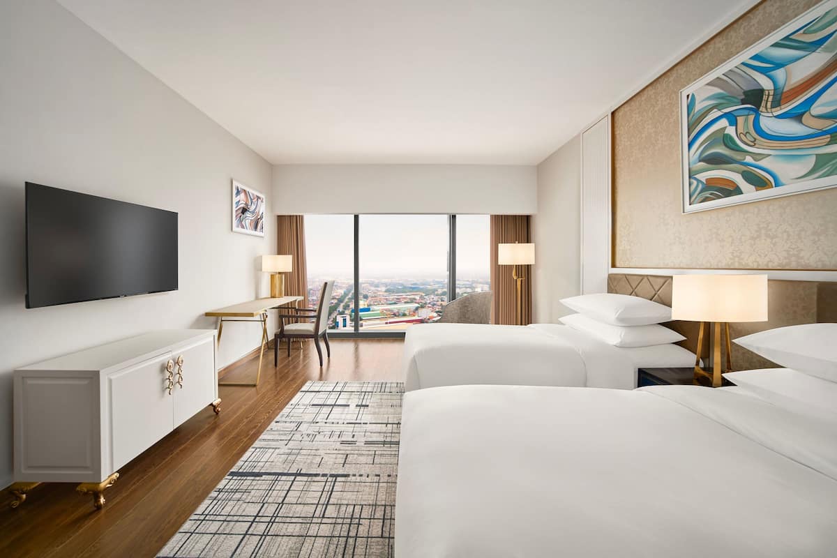 Ett hotellrum med en stor säng, ett skrivbord, en stol, en TV och utsikt över staden.