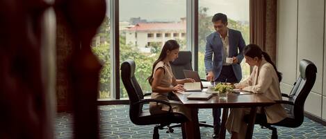 A conference room with a large window, a table with documents, and three people engaged in a discussion.
