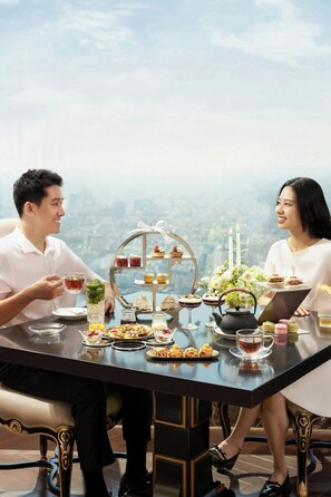 A couple dining at a table with a dessert display and candles, overlooking a cityscape. - Sheraton Hai Phong (Hai Phong)