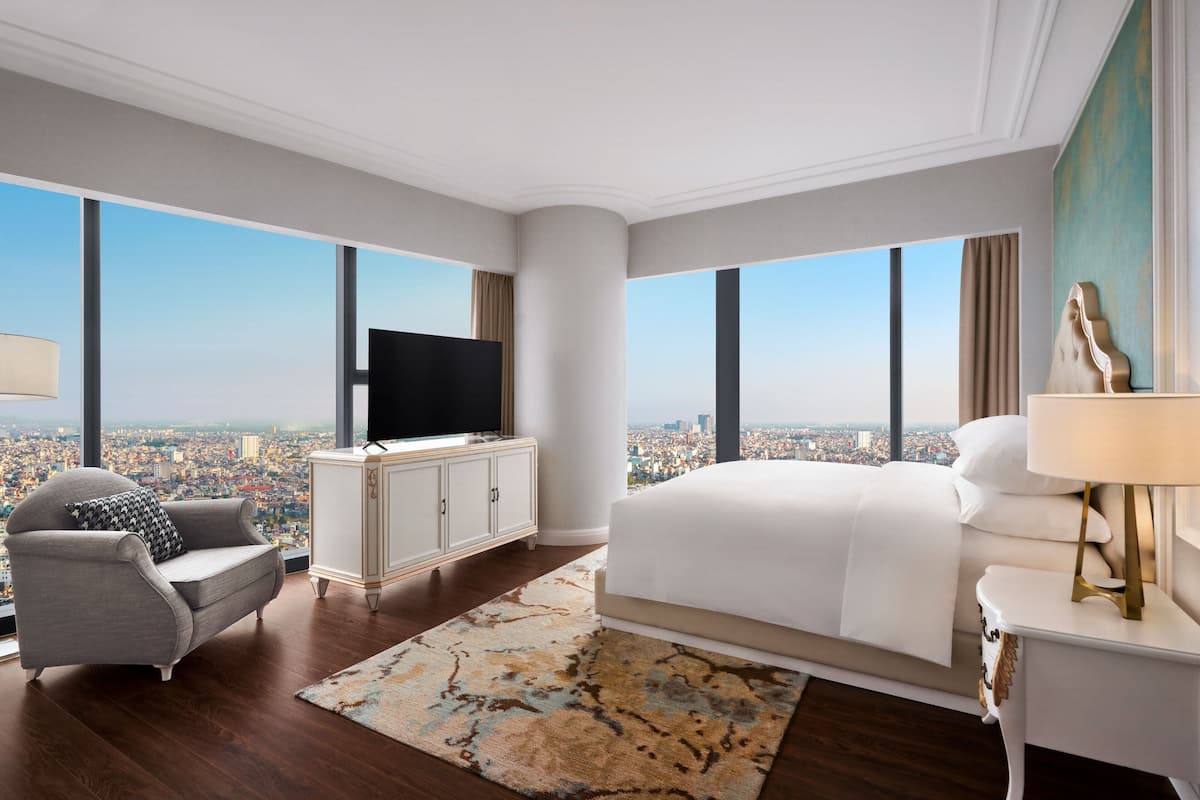 Ett modernt hotellrum med en stor säng, en TV, en soffa och utsikt över staden.
