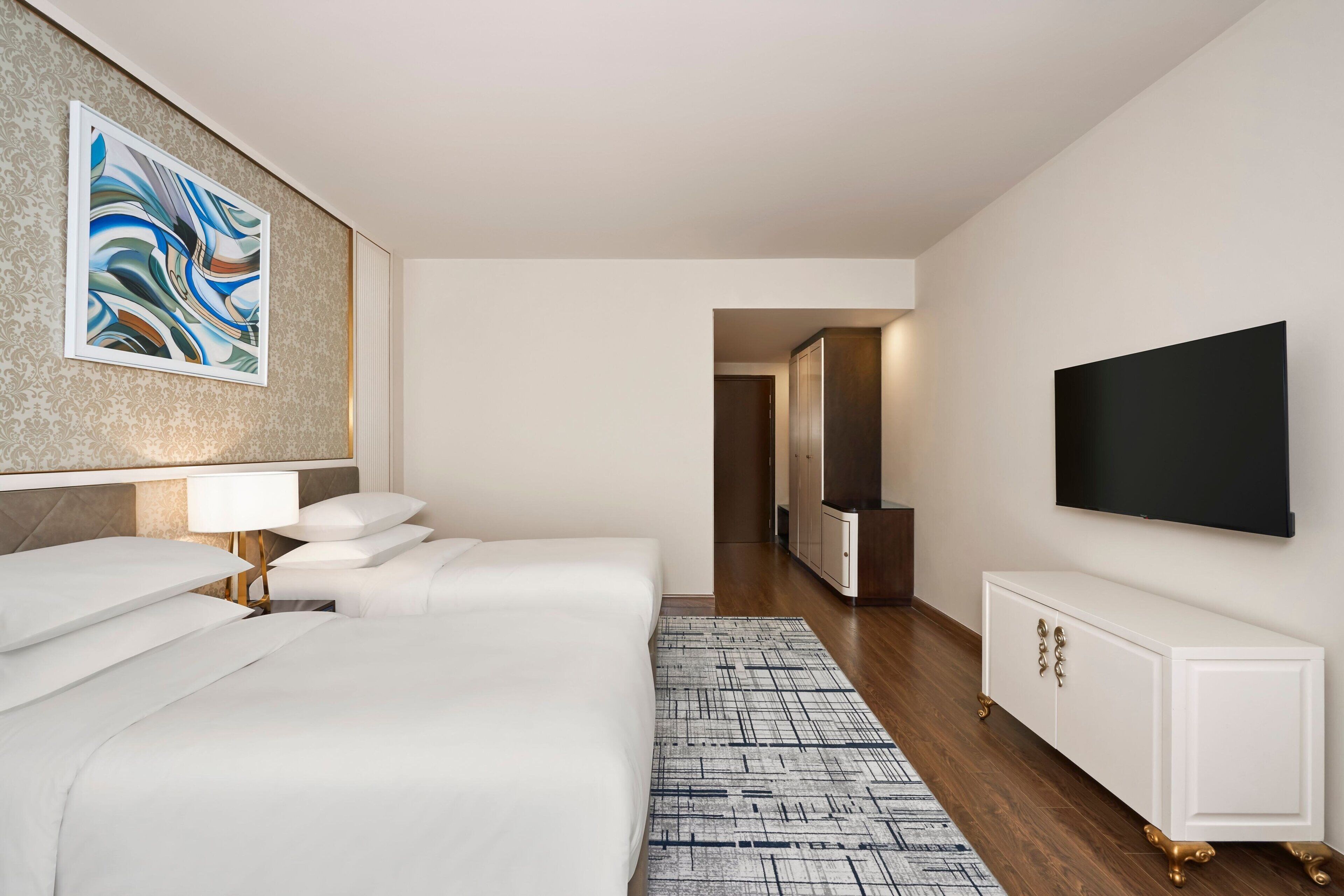 A hotel room with a large bed, a TV, a cabinet, and a painting on the wall.