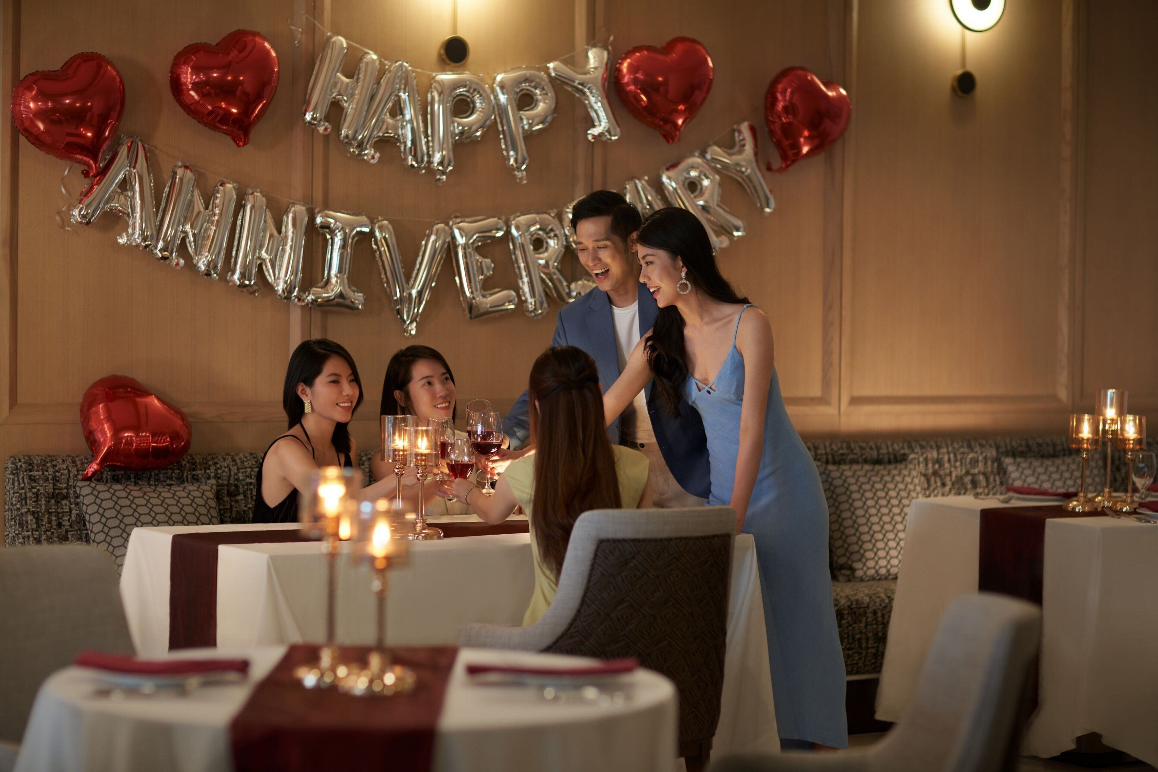 Un comedor con mesas redondas, velas y globos con forma de corazón.