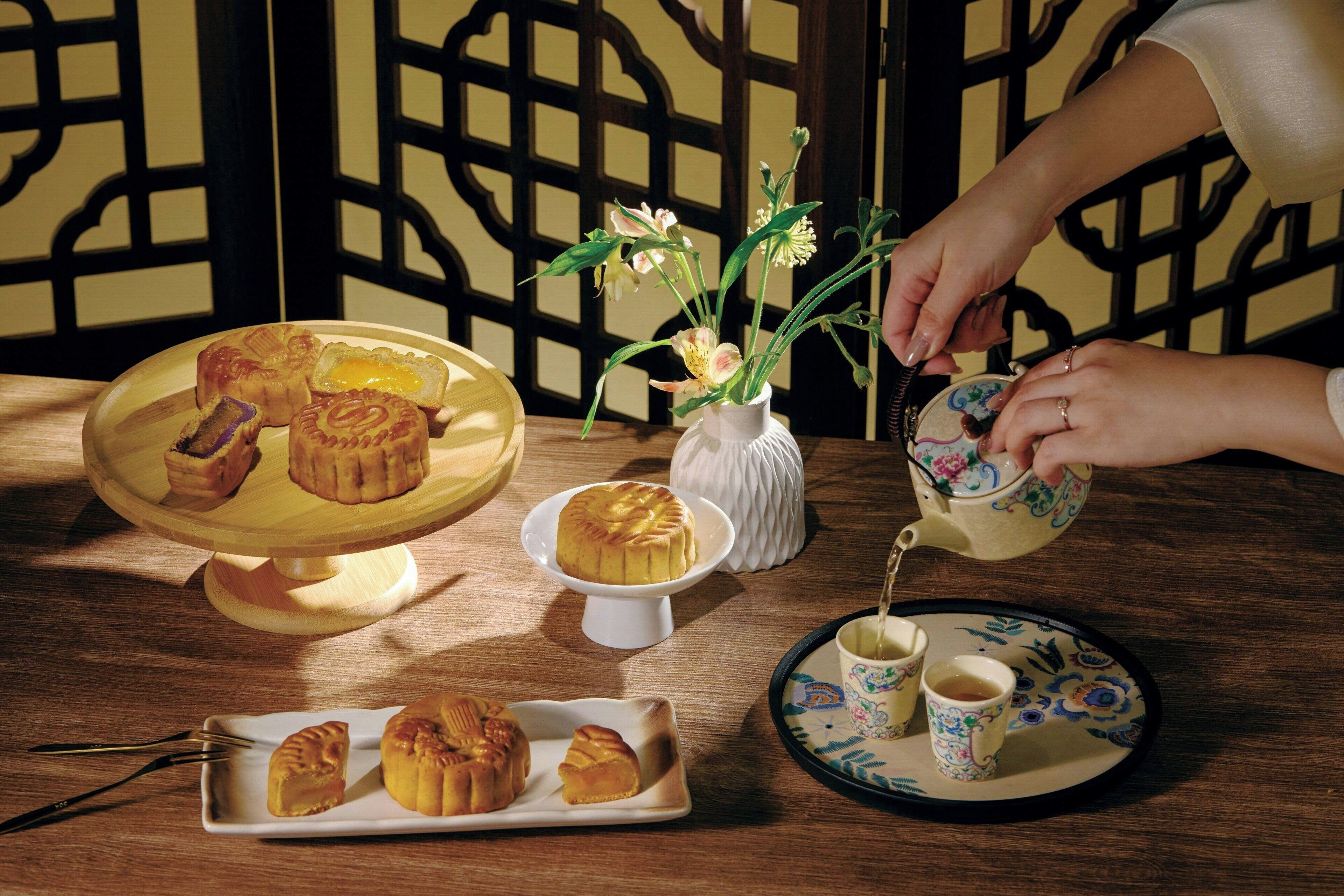Uma mesa com doces, um bule de chá e um vaso de flores.