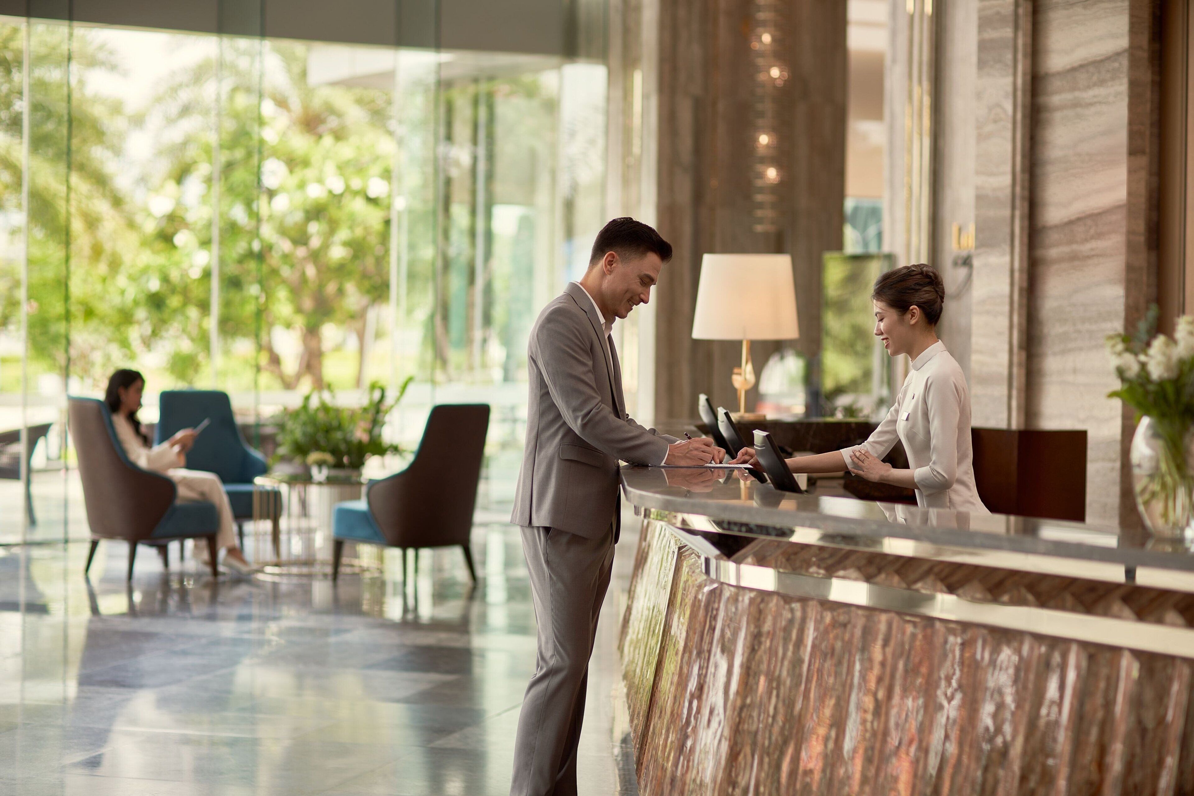 A reception area with a marble counter, seating, and a view of greenery outside.