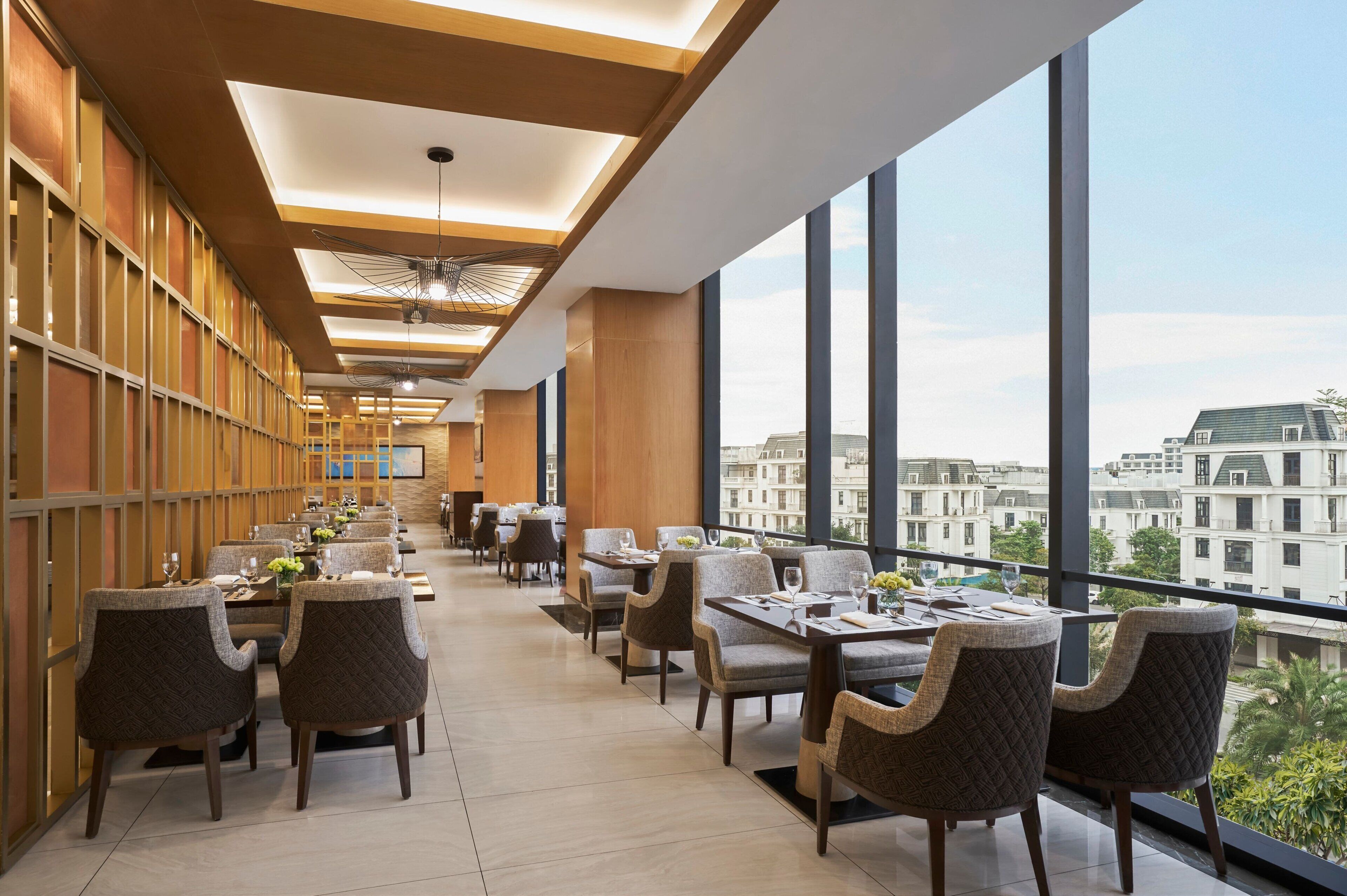 A modern dining area with high ceilings, large windows, and a view of buildings.