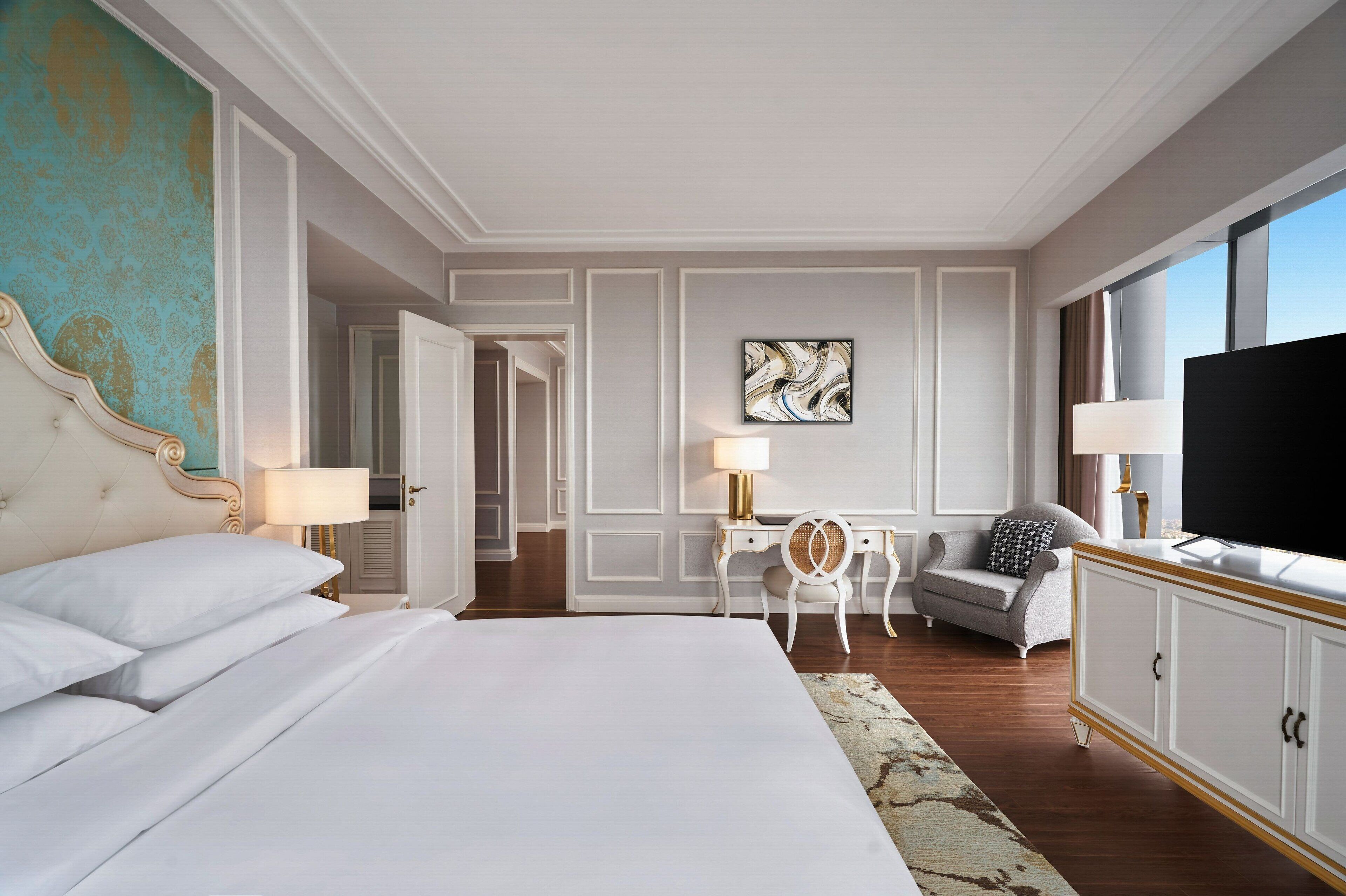 Una camera d'albergo con un letto grande, una scrivania con una sedia, un divano, una televisione e un'ampia finestra.