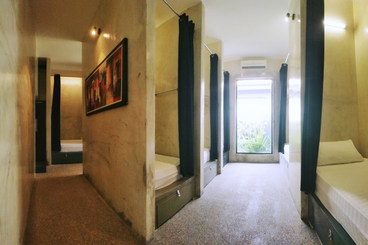 Une chambre d’hôtel avec un lit, un petit bureau, une chaise, une fenêtre avec des rideaux et un tableau au mur.
