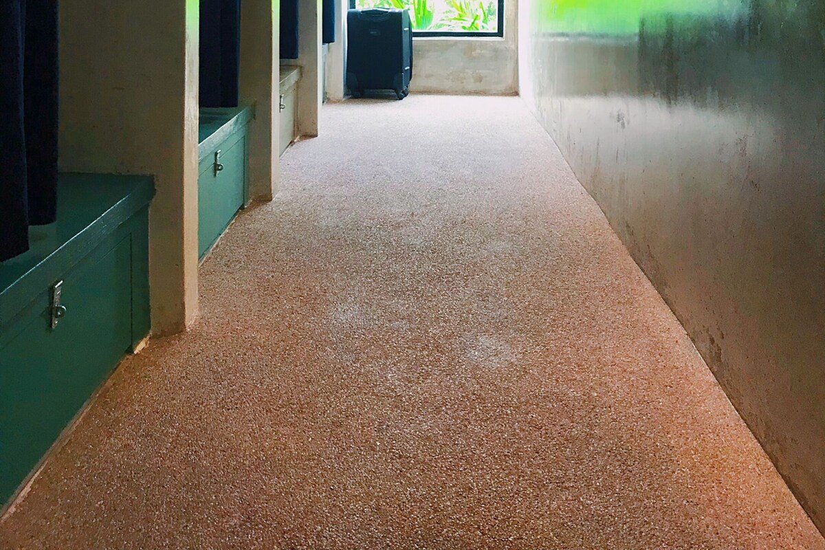 Un couloir avec une grande fenêtre, une valise et un meuble vert.