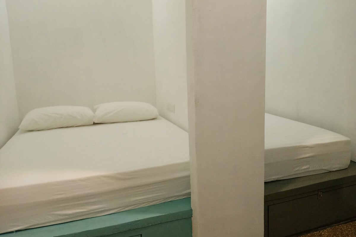Un lit simple avec une literie blanche, dans une pièce aux murs de couleur turquoise et ornée d’un pilier blanc.