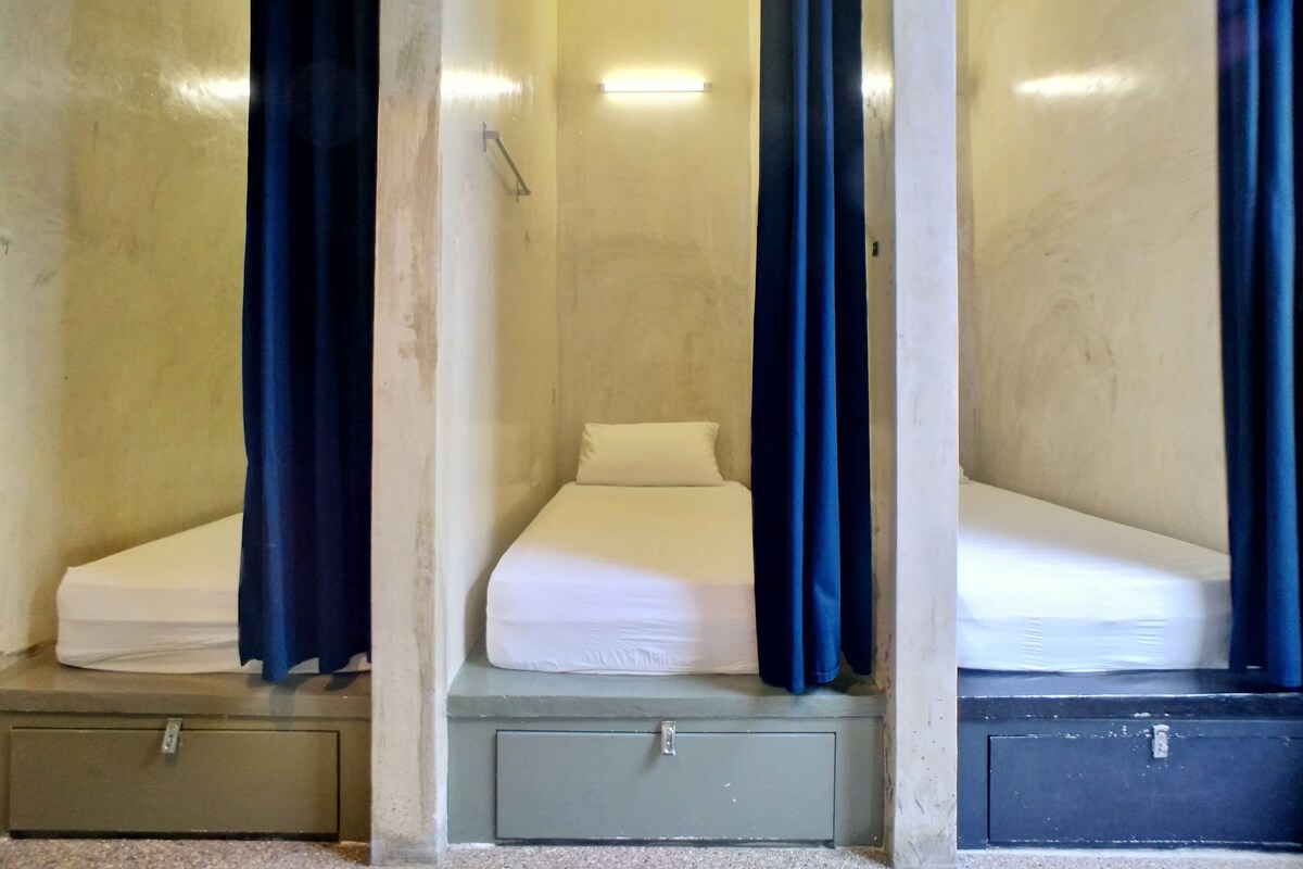 Trois lits simples avec des rideaux bleus, chacun étant équipé d’un matelas et d’un petit tiroir en dessous.