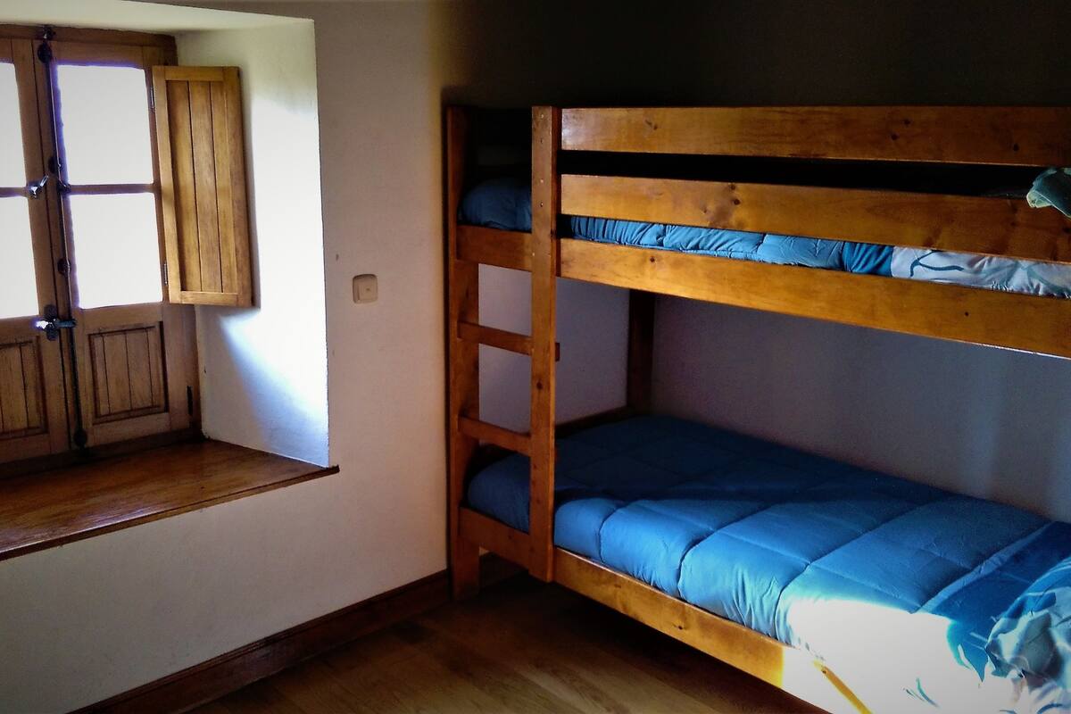 A bunk bed with blue bedding, a wooden bench, and a window with a wooden shutter.