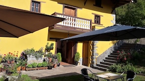 A yellow building with a balcony, outdoor seating, and potted plants.