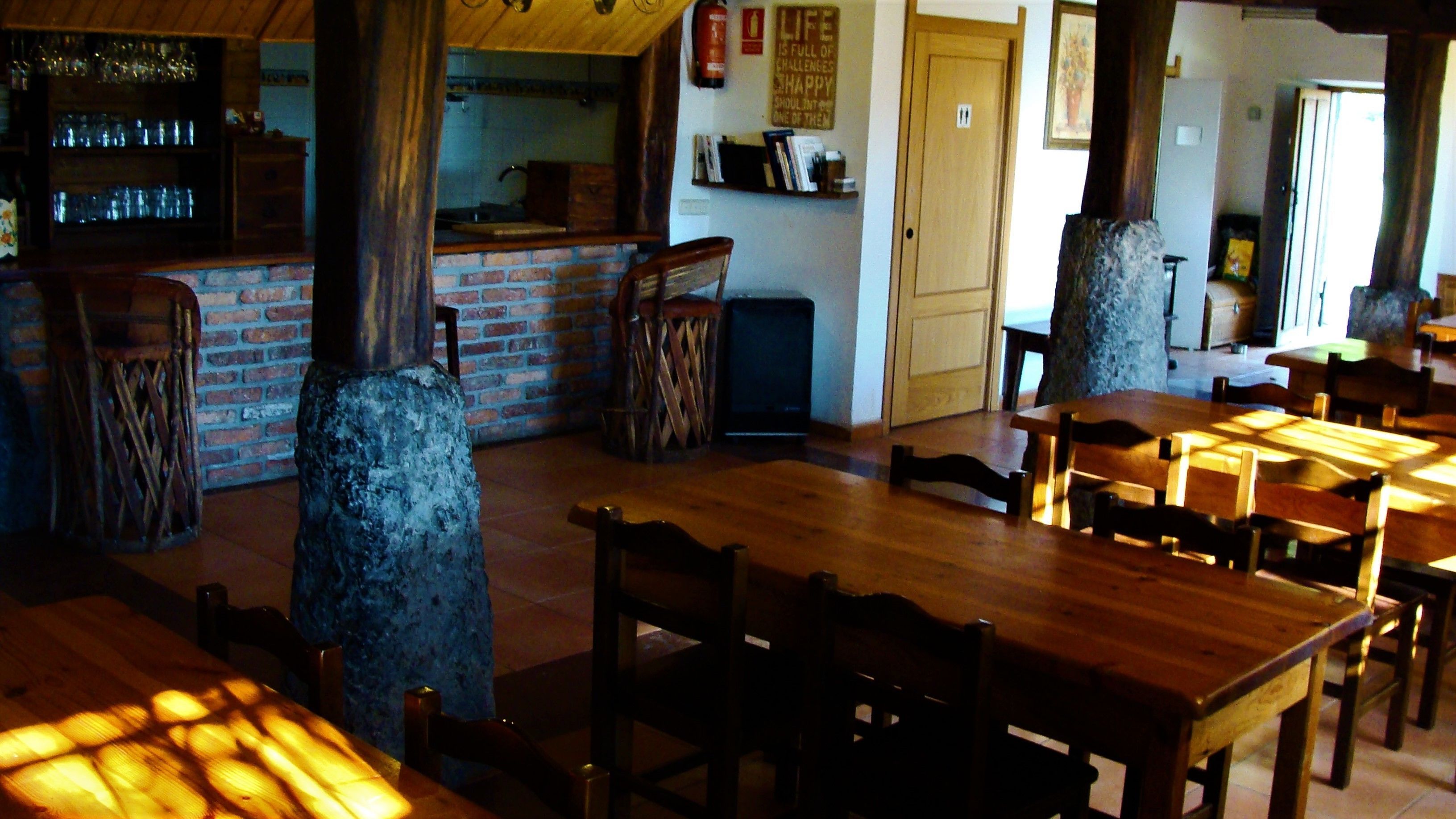 Un intérieur rustique avec des tables et des chaises en bois, un mur en briques et un coin bar avec des étagères remplies de verres.