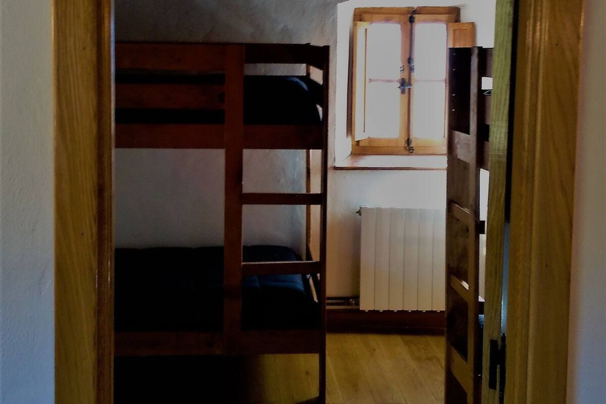 A narrow hallway with a wooden bunk bed on the left and a window with a wooden frame on the right.