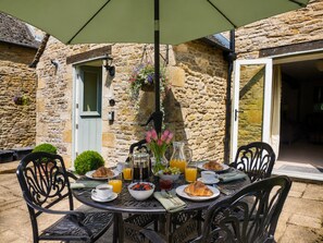 A stone building with a dining table set for breakfast, including croissants, fruit, and beverages.