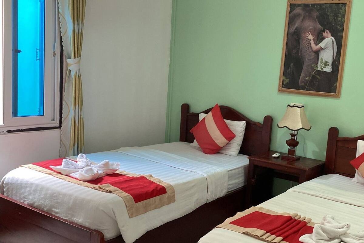 Two single beds with red and white pillows, a bedside table with a lamp, and a framed picture on the wall.