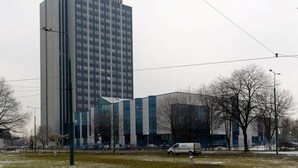 A tall modern building with a glass facade, surrounded by a park with bare trees and a parked van. - Komplex Apartamenty Europa Sosnowiec (Sosnowiec)
