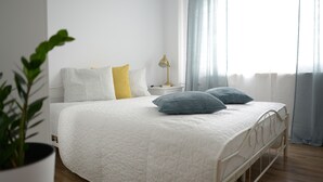 A neatly made bed with a white quilt, two pillows, a bedside lamp, and a potted plant. - Komplex Apartamenty Europa Sosnowiec (Sosnowiec)