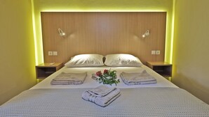 A neatly made bed with folded towels, a vase with flowers, and bedside tables with lamps. - Village chania (Platanias)