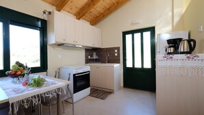 A compact kitchen with a dining area, featuring a wooden ceiling, white cabinets, and a refrigerator with a coffee maker. - Village chania (Platanias)