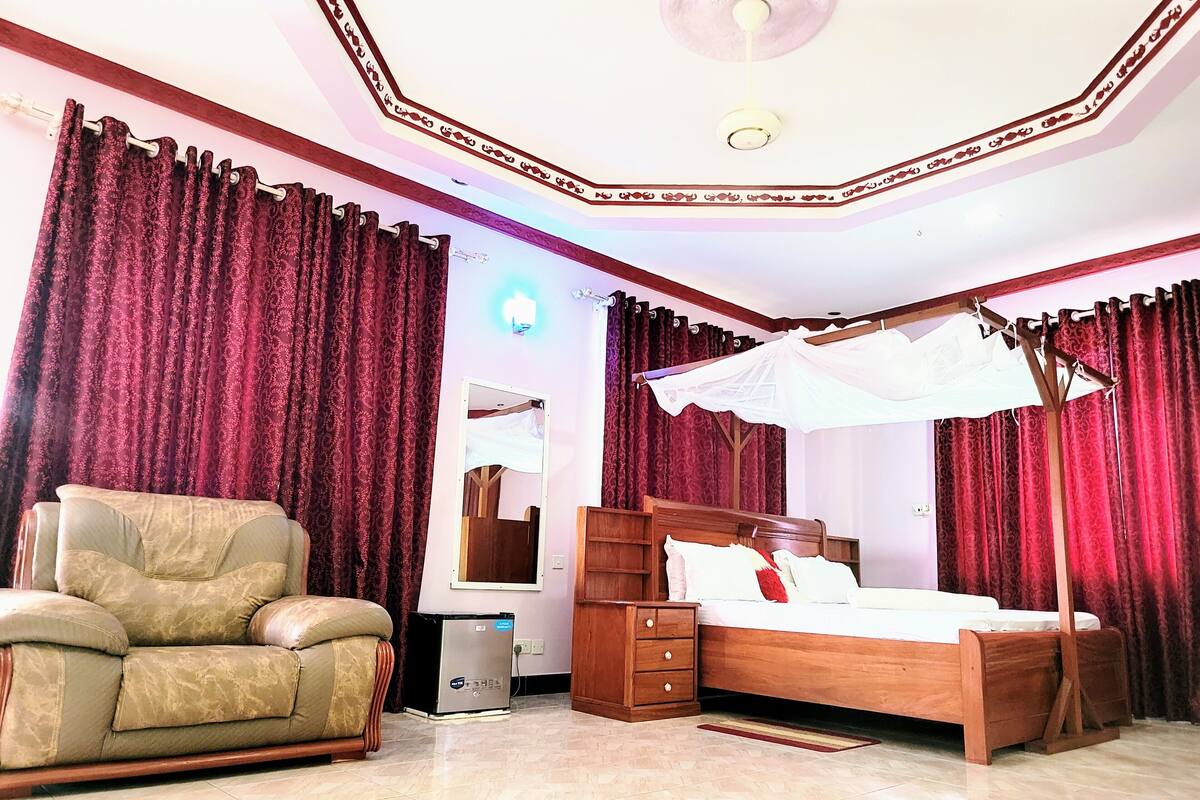 Une chambre à coucher comprenant un lit, une chaise, une table de chevet, un miroir et un ventilateur de plafond.