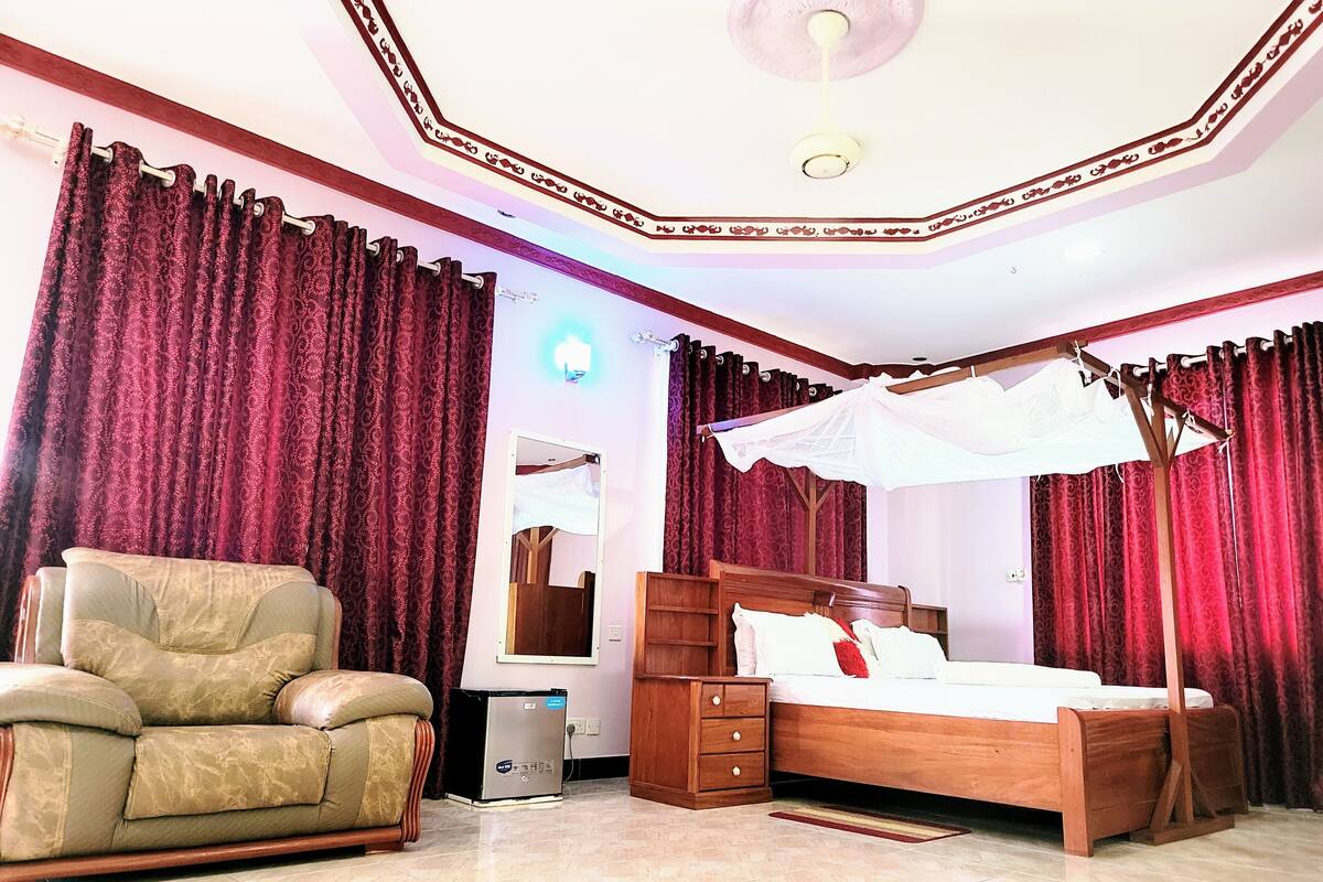 Une chambre à coucher comprenant un lit, une chaise, une table de chevet, un miroir et un ventilateur de plafond.