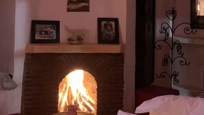 A cozy room with a fireplace, a bed, a table, and a wall-mounted picture. - Auberge Ayam Atlas (Ourika)